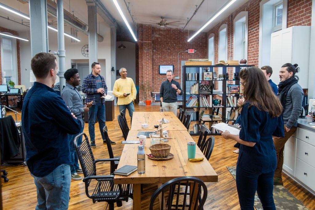 Team members standing around large table in a refurbished industrial open office setting