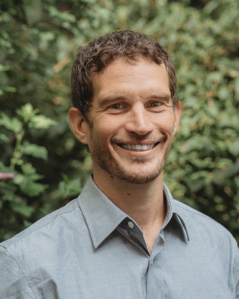 Dan Bowden, smiling wearing a grey button up.