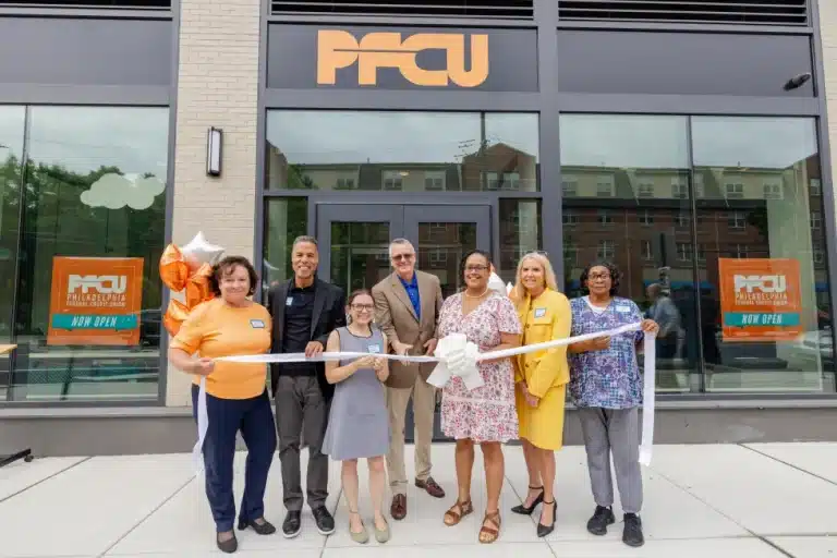 Group of people doing a ribbon cutting ceremony in front of a new PFCU branch opening.