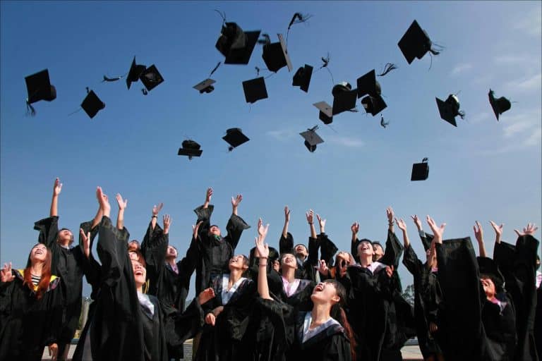 Several students in graduation gowns throwing their caps in the air in celebration.